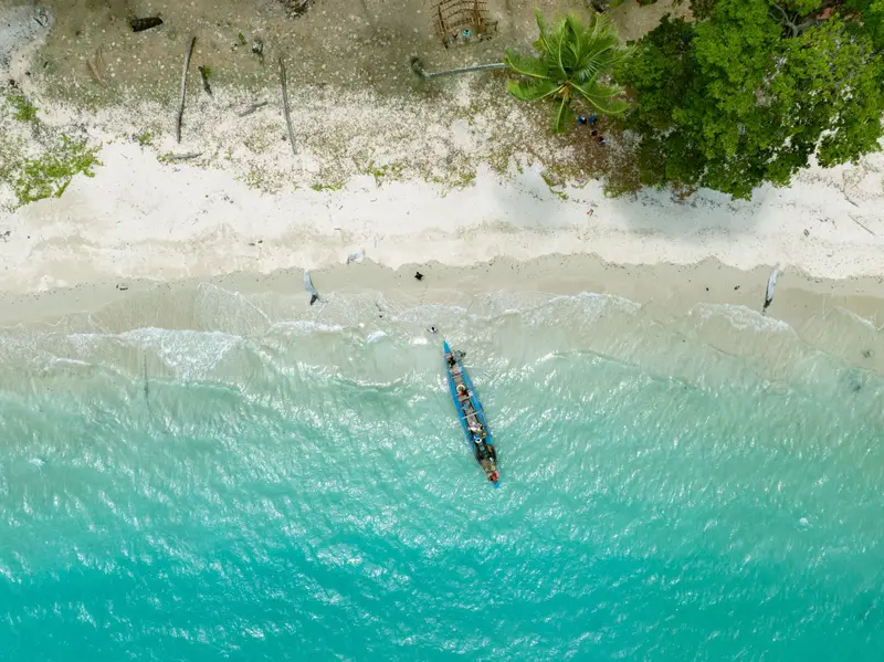 Aerial view of a boat on turquoise water off a forested beach on Long Island, Andaman