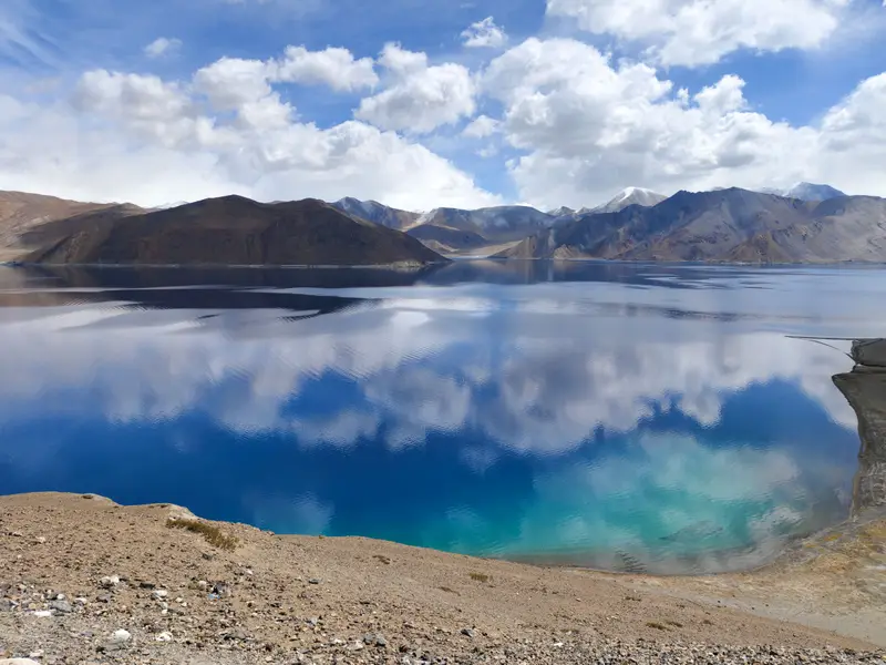 Mountains and clouds reflected in the still blue water of Pangong Lake, Ladakh