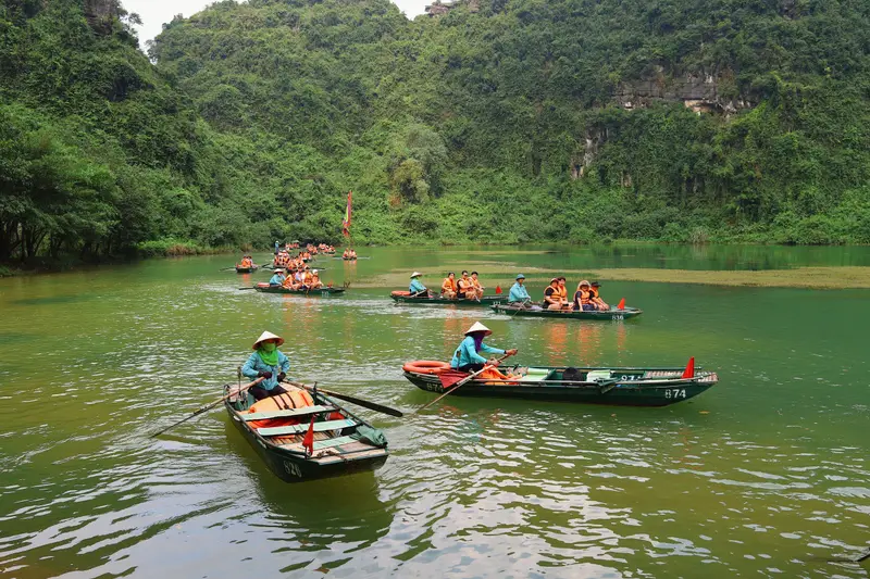 Rowing boats on the green river between forested limestone hills at Trang An, Hoa Lu, Ninh Binh, Vietnam